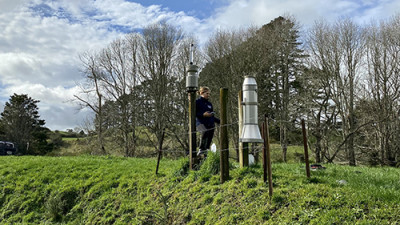 Image of a lady standing in a field next to a rain gauge