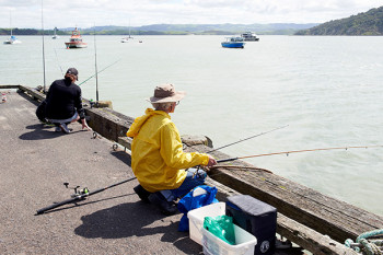 Behind the fishermen on the wharf is a collection of vessels on swing moorings in the Raglan harbour.